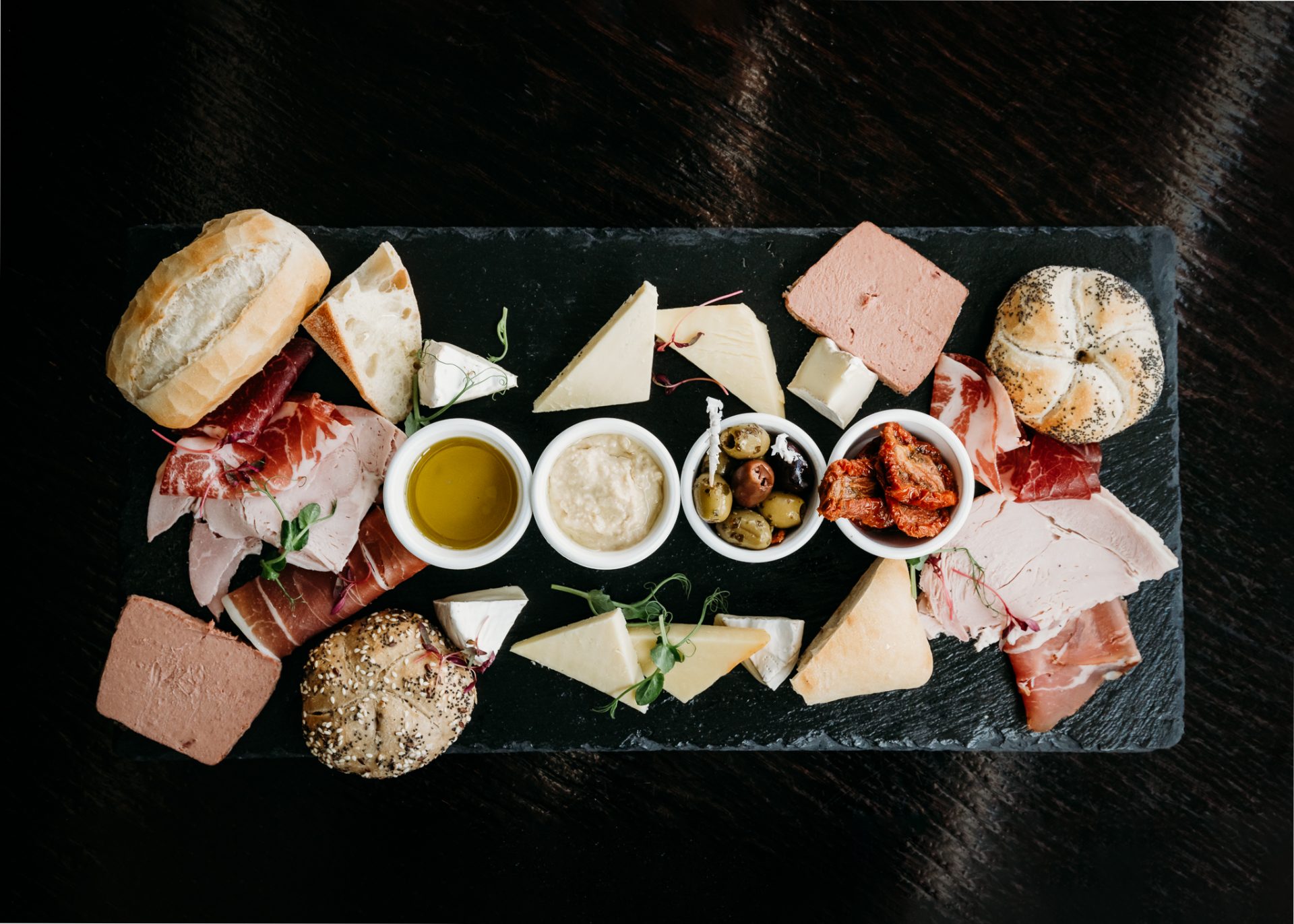 food platter with breads, sundried tomatoes, olives, oil, hummus, cheese, meats and pate