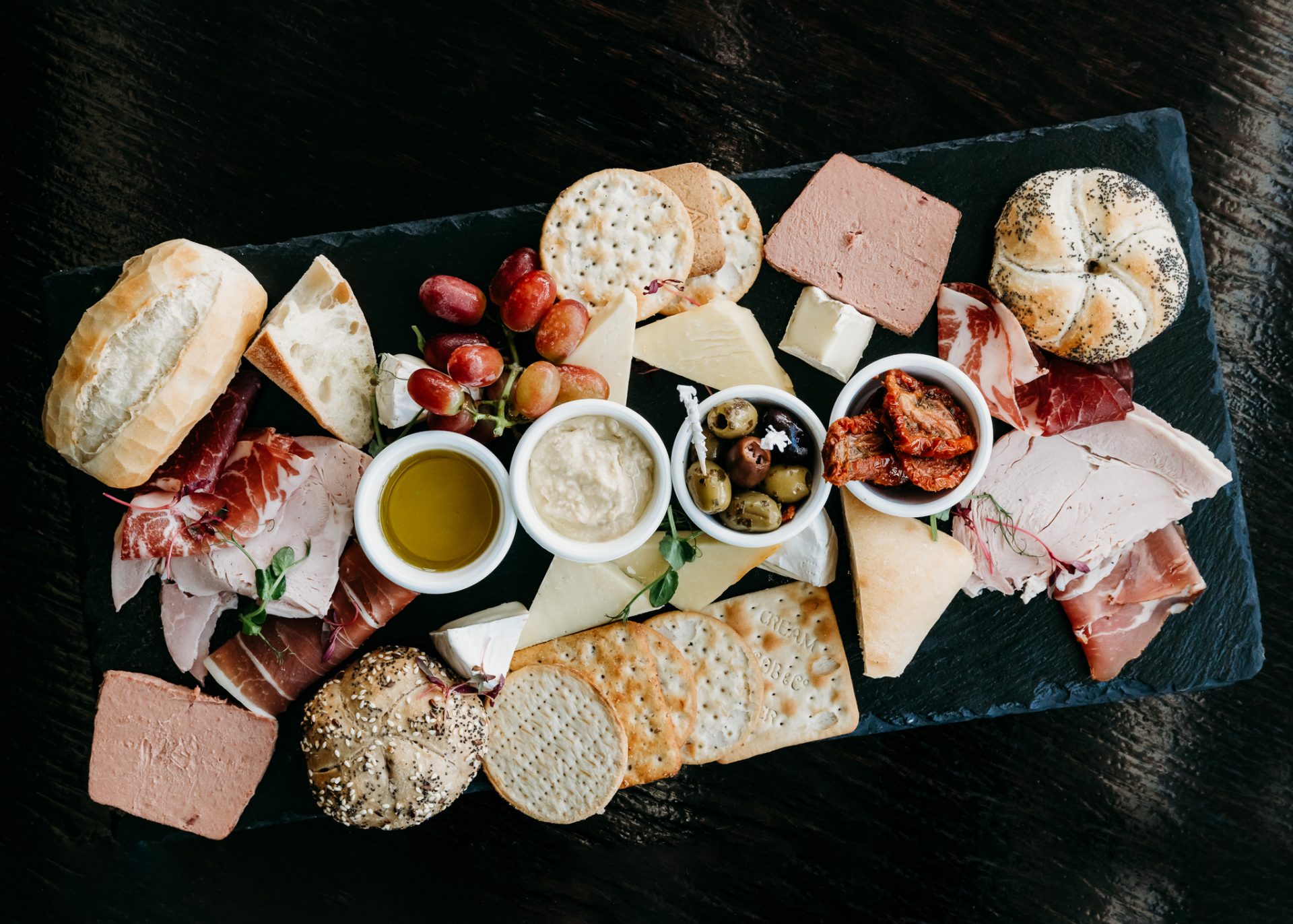 food platter with breads, meats, sundried tomatoes, crackers, grapes and dips