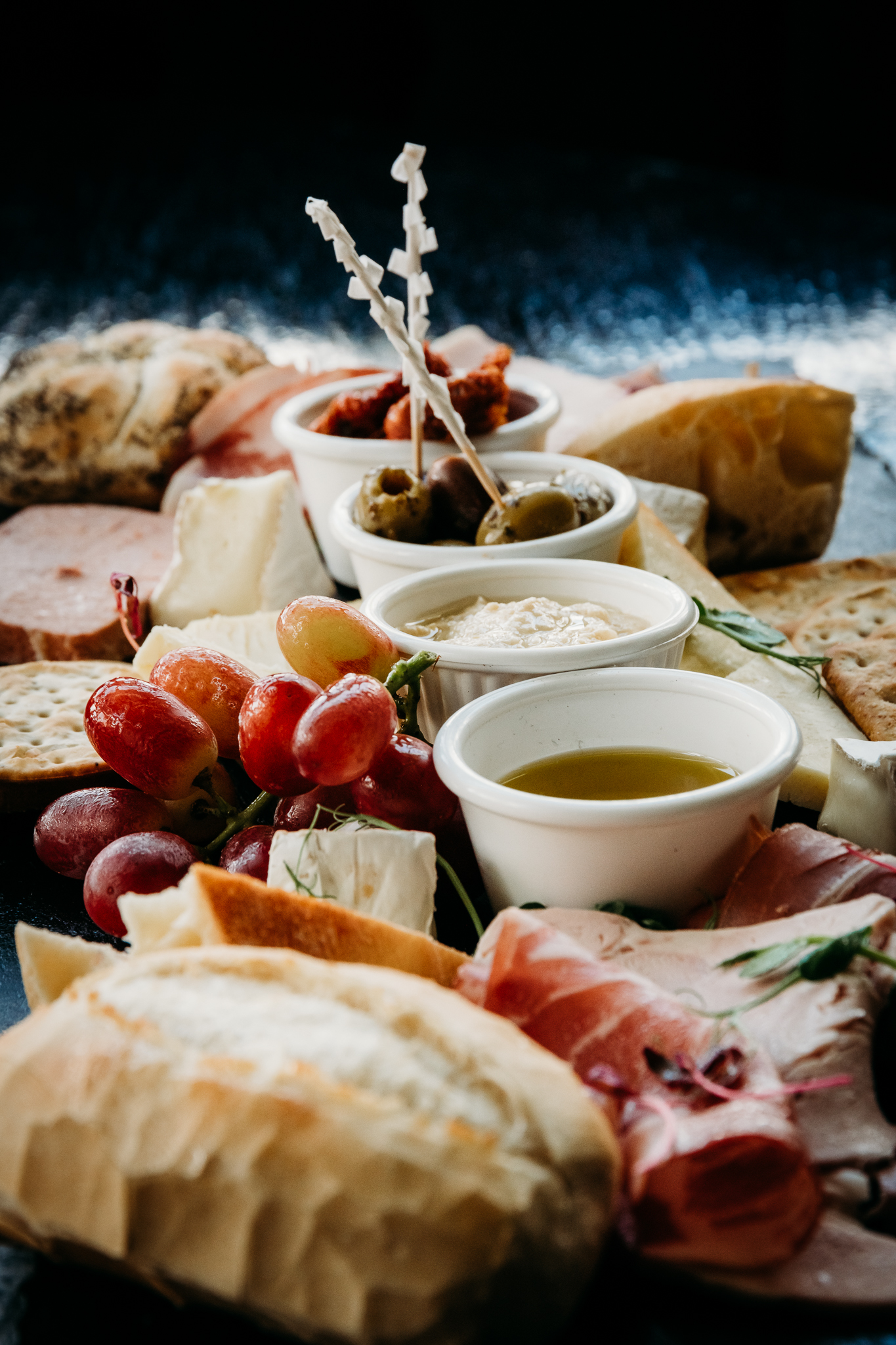 food platter with grapes, breads and meats along with four different dips and olives in the centre