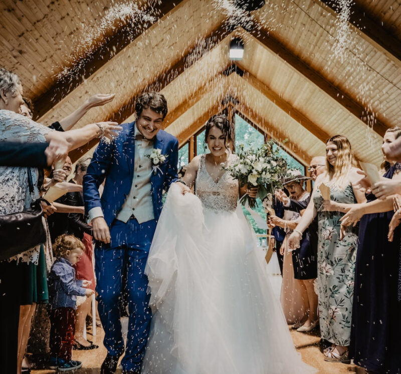 bride and groom walking towards camera with guest throwing rice over them