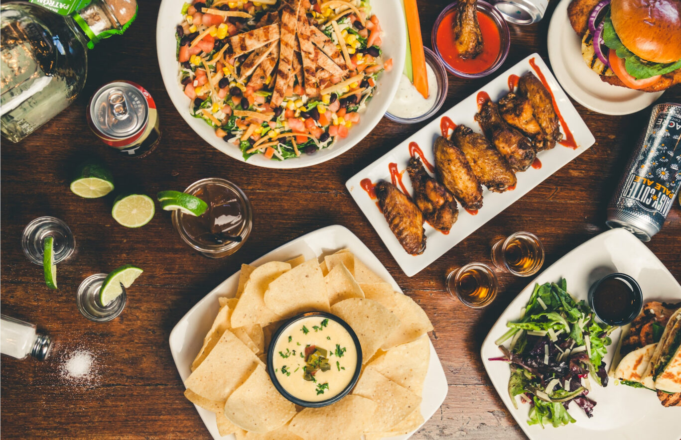 Food platters, chicken wings, chicken salad, a can of coke, shot glasses with tequila, burgers, dips and wraps