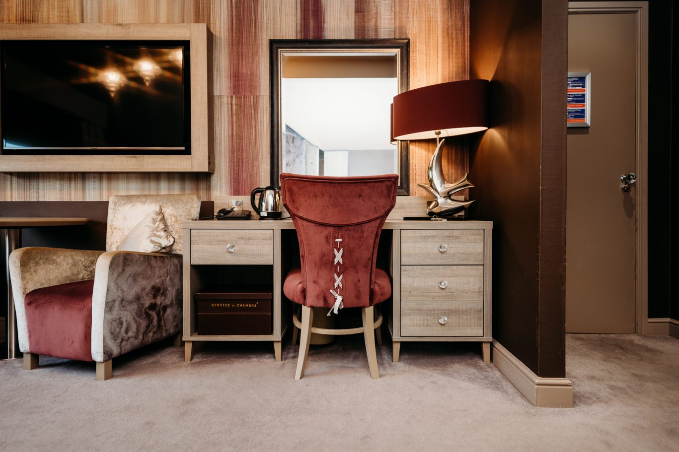 Red Hall Hotel bedroom with burgundy wing backed chair and lamp with gold and burgundy arm chair