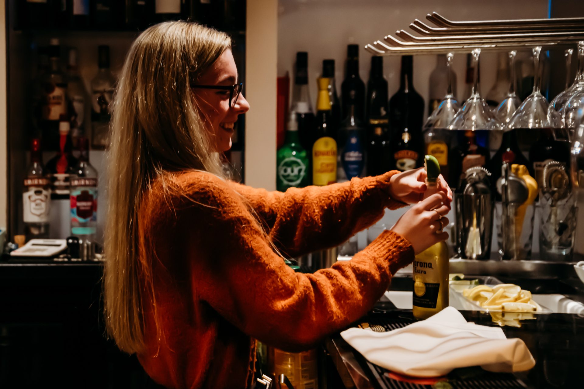 Red Hall Hotel bartender wearing an orange jumper putting a lime into a corona bottle