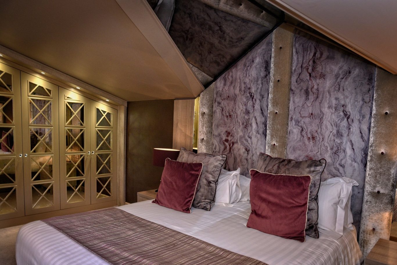 large hotel bedroom with large headboard burgundy cushions and a runner at the end of the bed