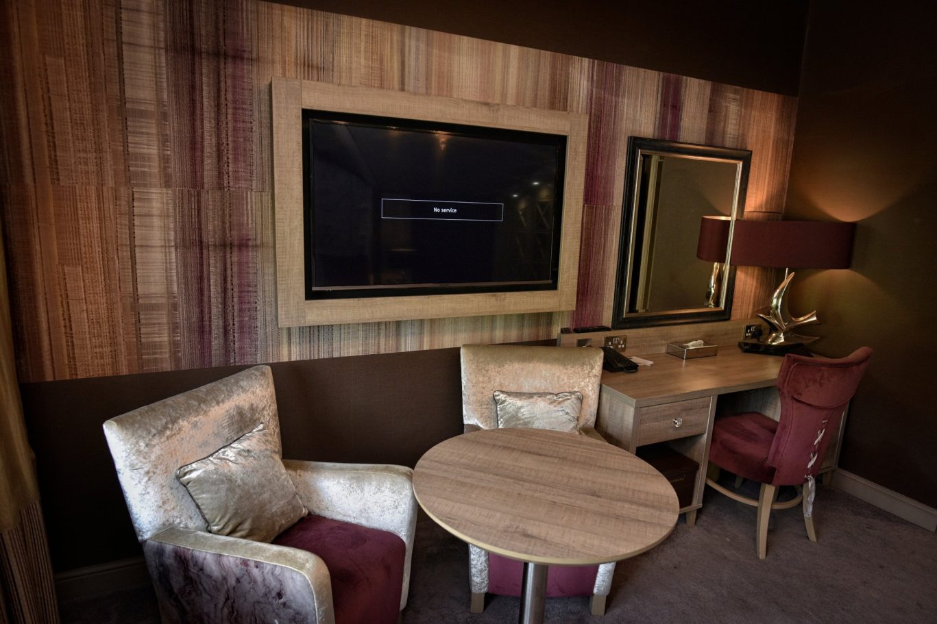 Seating area in bedroom, with two lounge chairs, burgundy chair in front of a dressing table and mounted large tv