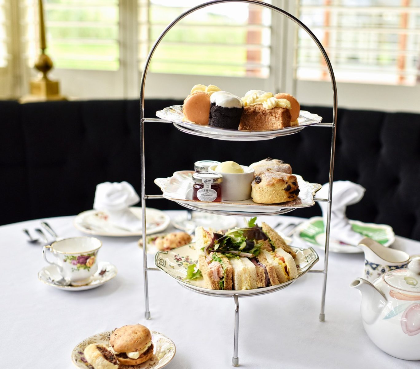 afternoon tea with sweet treats at the top later, scones and jam on the middle and a selection of sandwiches on the bottom