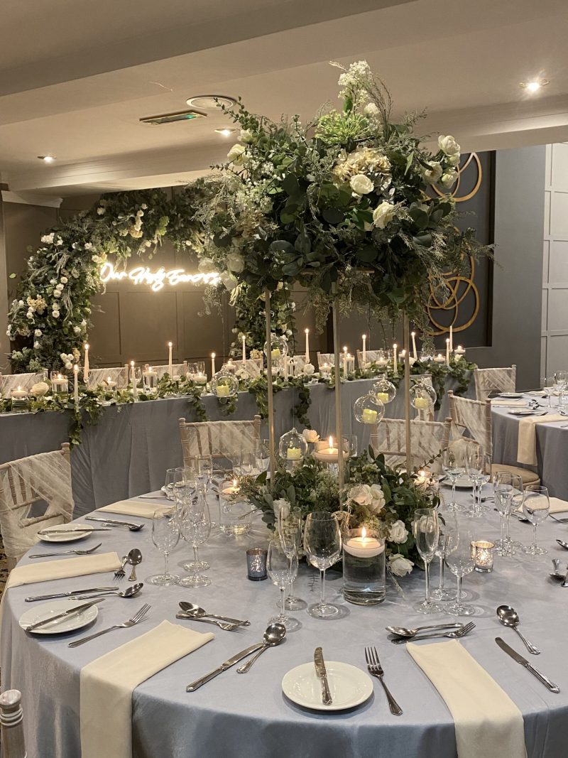 round table set up for wedding with light blue table cloths and foliage centre piece with golden stands