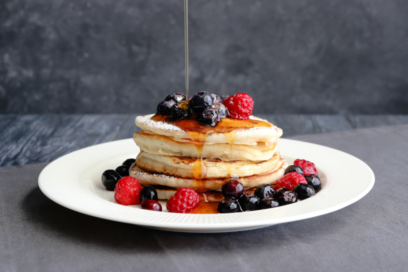 american style pancakes stacked with berries and maple syrup dripping from the top of the page
