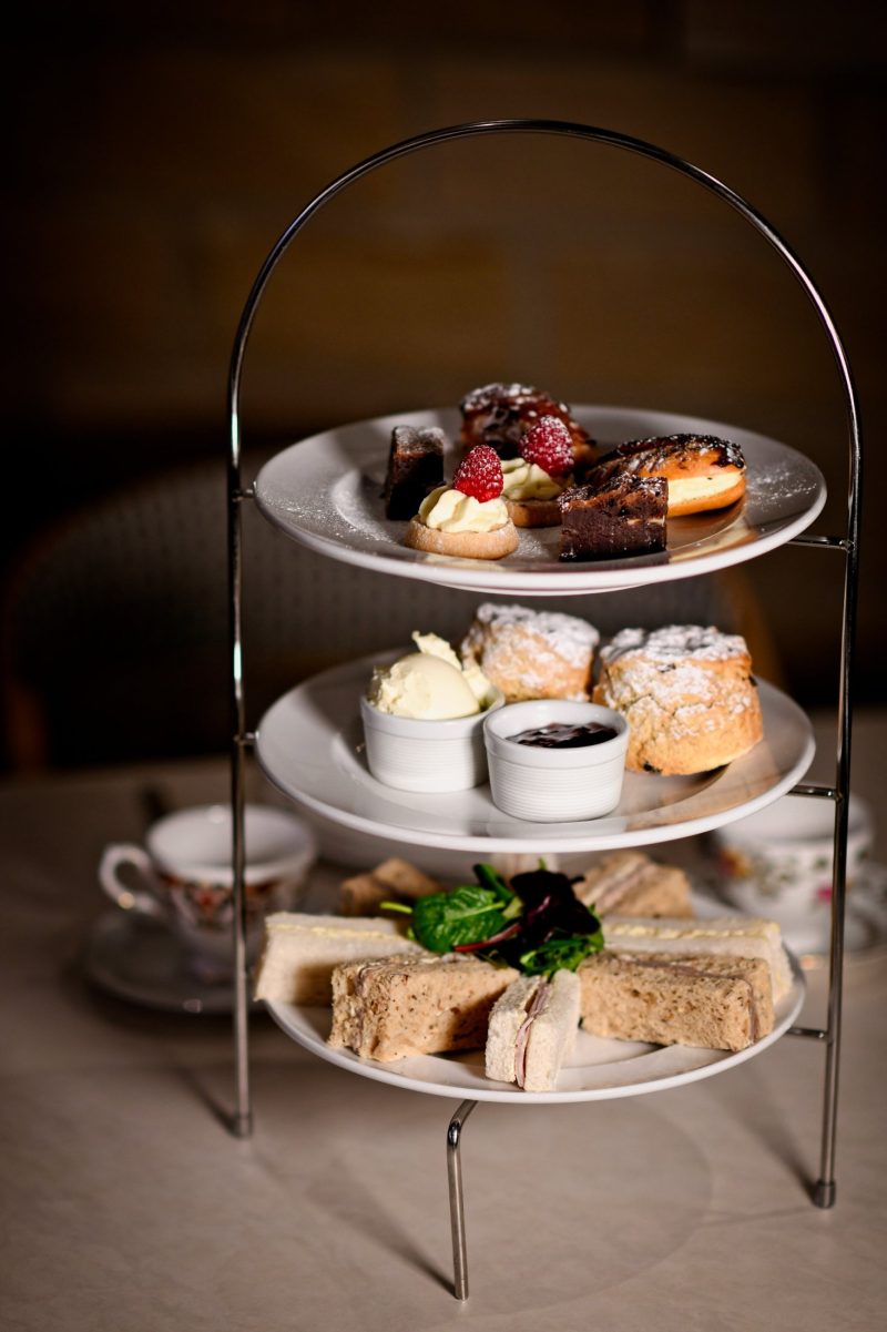 afternoon tea with cakes on the top layer, scones and jam on the middle, the bottom layer with an assortment of sandwiches on white and brown bread