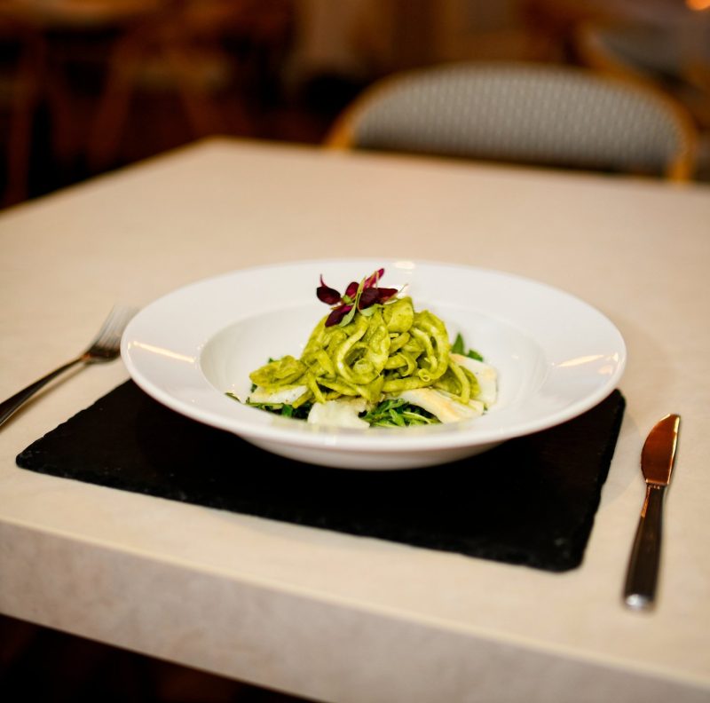 pesto pasta halloumi dinner in a wide rimmed bowl sat on the table set for one person