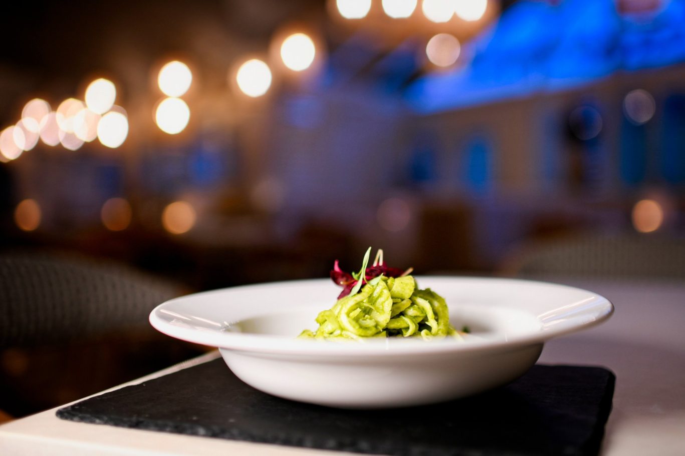 large bowl of pesto pasta with halloumi, background of lights and blurry