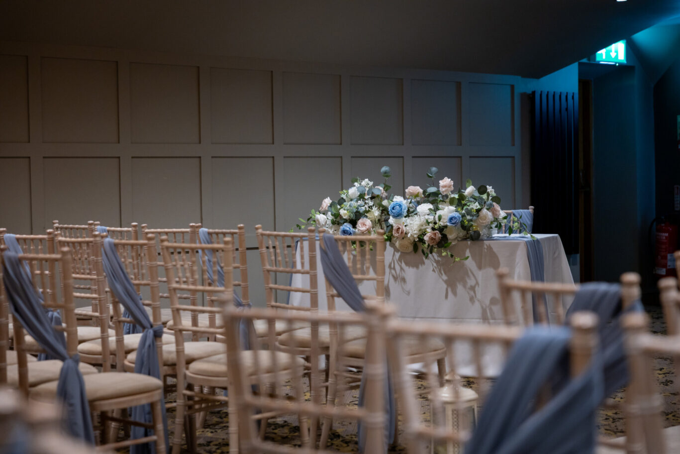 Modern and beautifully furnished wedding ceremony room with panelled walls, sashed chairs for guests, and large flower arrangement for a wedding ceremony at Red Hall Hotel in Greater Manchester.