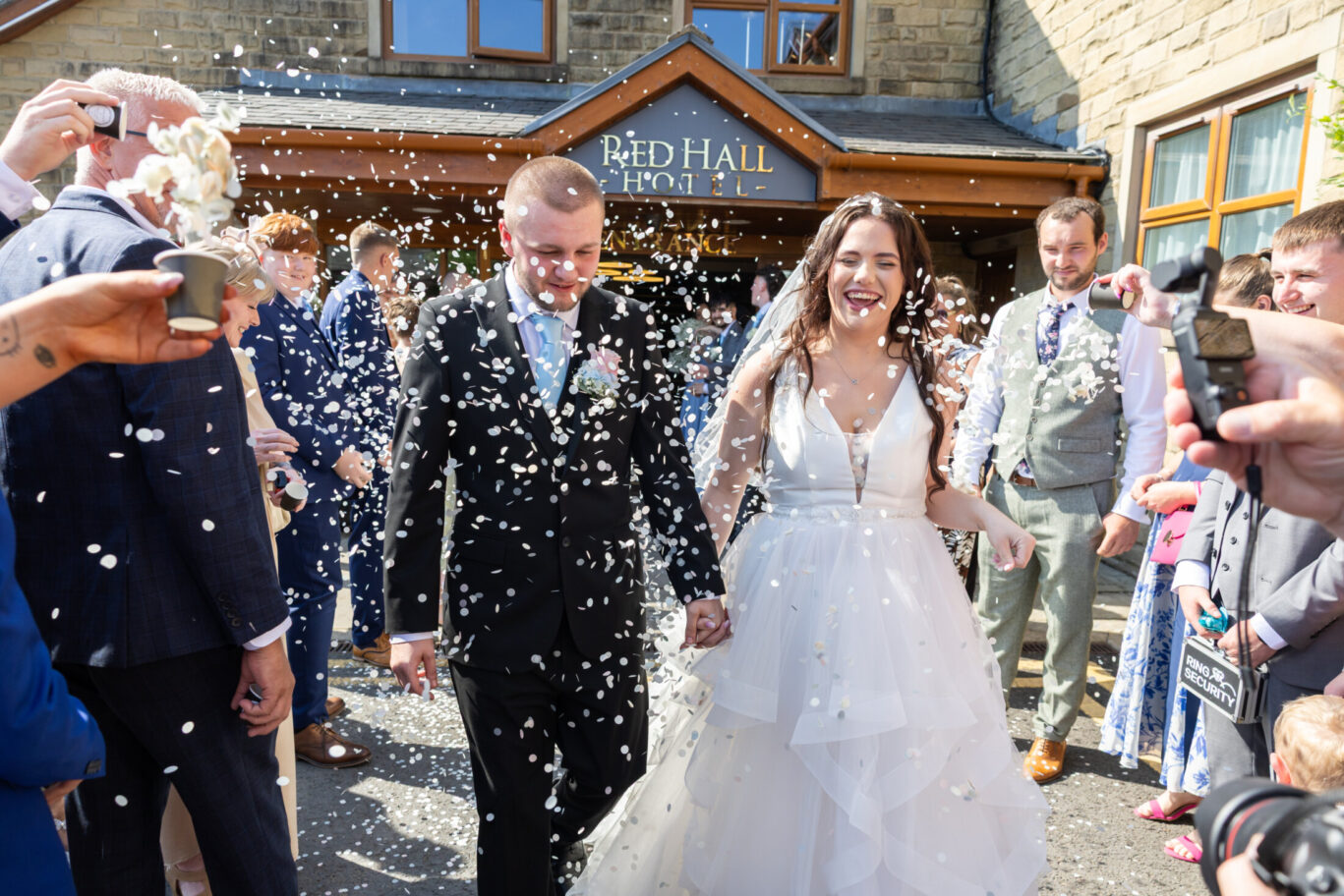 Bride and groom with wedding guests throwing confetti outside the Red Hall Hotel entrance in Bury.