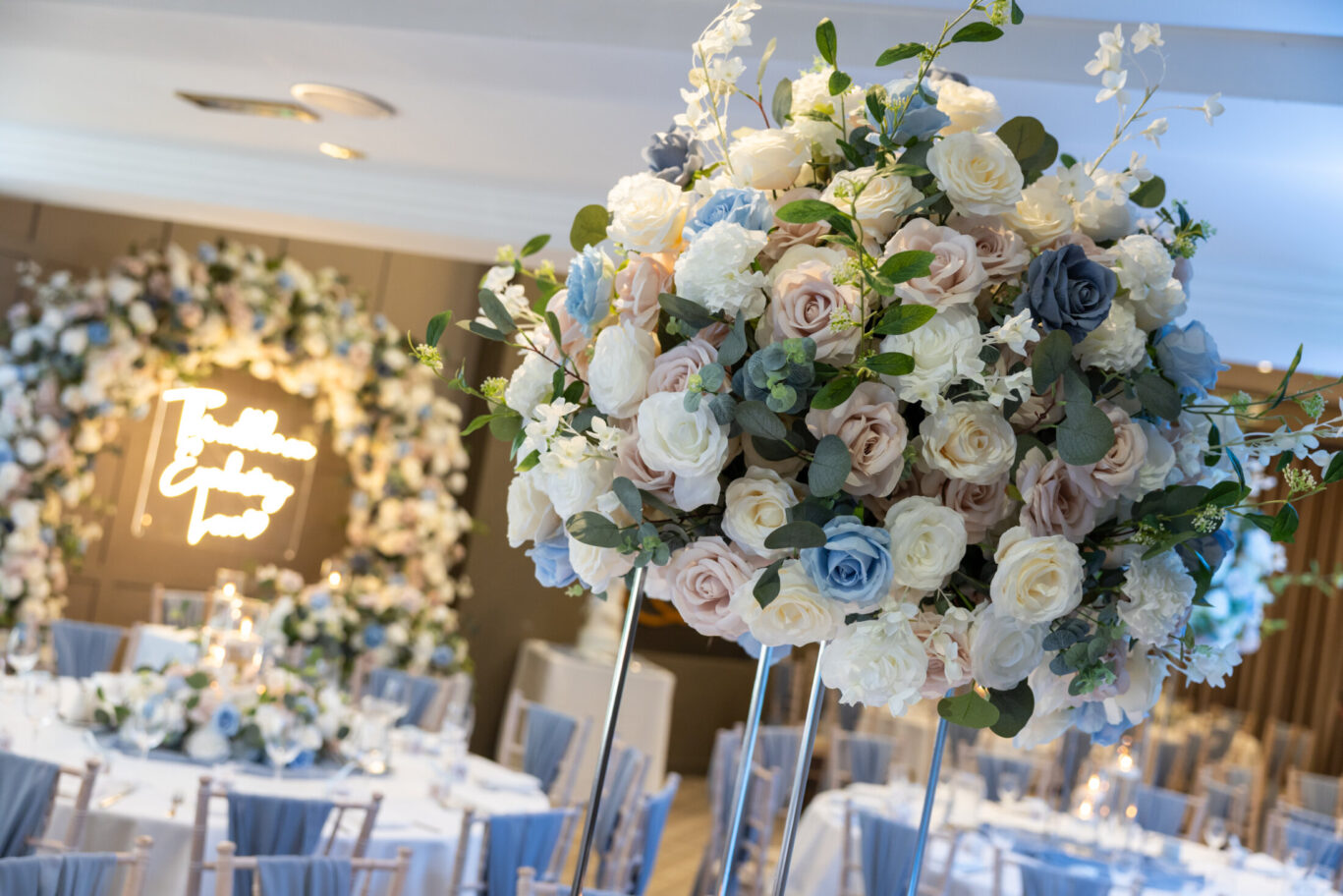 Flower centrepiece decoration on a wedding table with soft lighting and a flower arch in the background during a wedding at Red Hall Hotel in Bury.